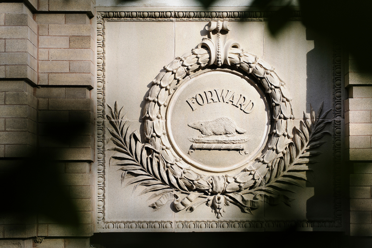 Tree foliage frames an architectural detail -- the state of the Wisconsin "forward" motto and an iconic image of a badger.